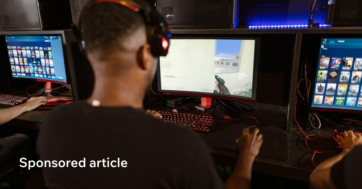 Person wearing a headset playing a first-person shooter game on a PC in a gaming center.